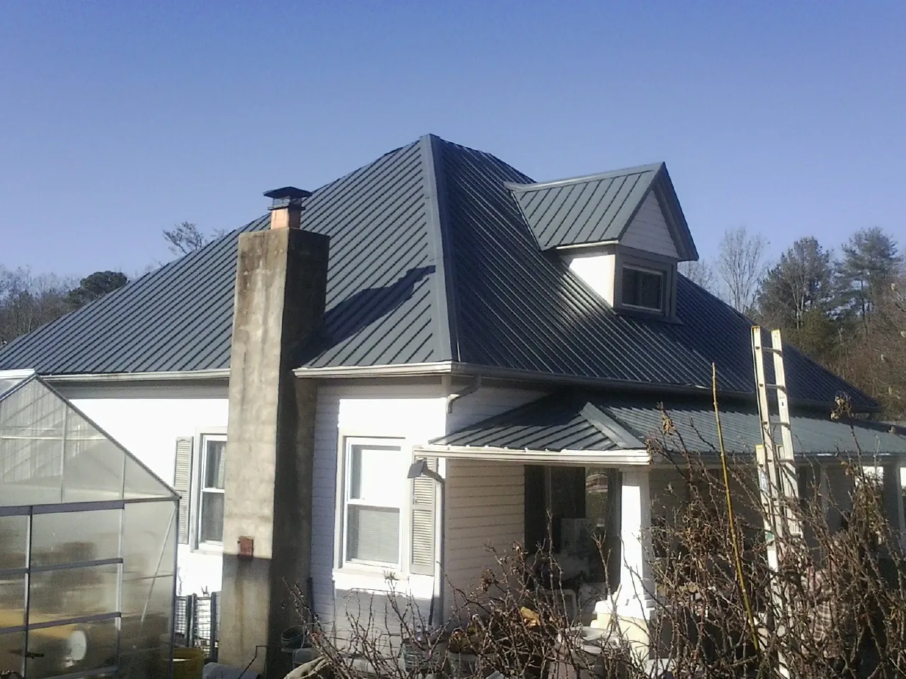 Dark blue standing seam metal roof on a white farmhouse with dormer — Slate & Tile Roof Repair by Roofing Brothers in Pitsburg