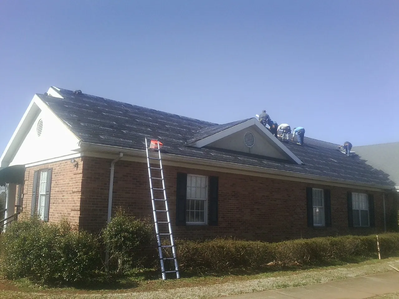 Crew tearing shingles off a brick ranch roof with a ladder set — Metal Roof Repair work by our crew in Pitsburg