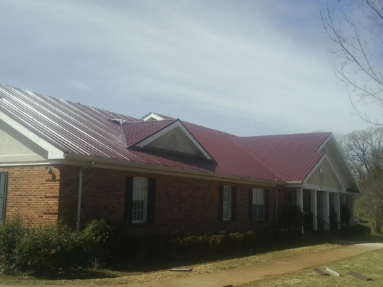 Red metal roof with gabled entries on a long brick building, from a Hail Damage Roof Repair job in Pitsburg