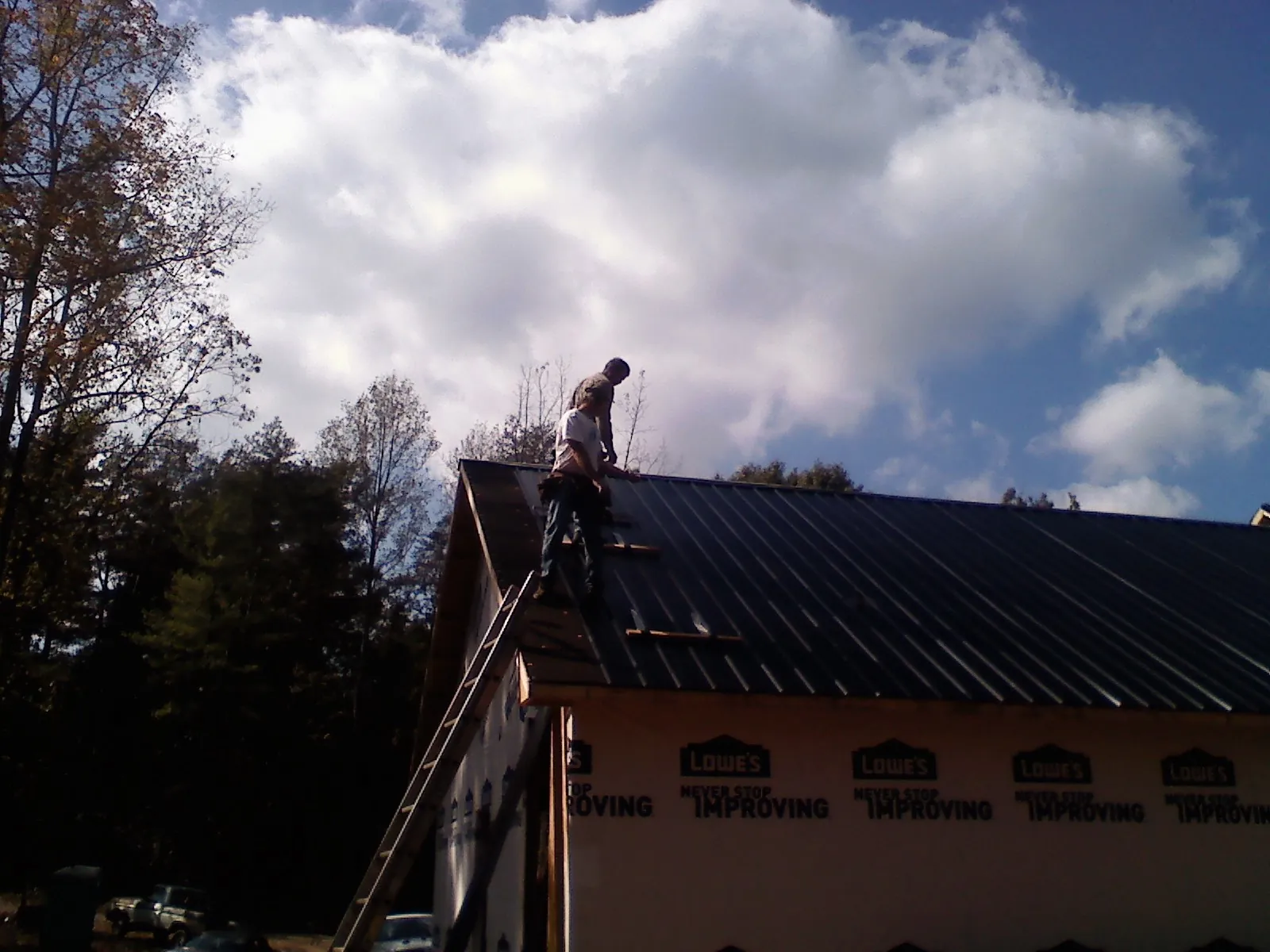 Roofer fastening dark metal panels high against a cloudy sky, from a Roof Inspection job in Pitsburg