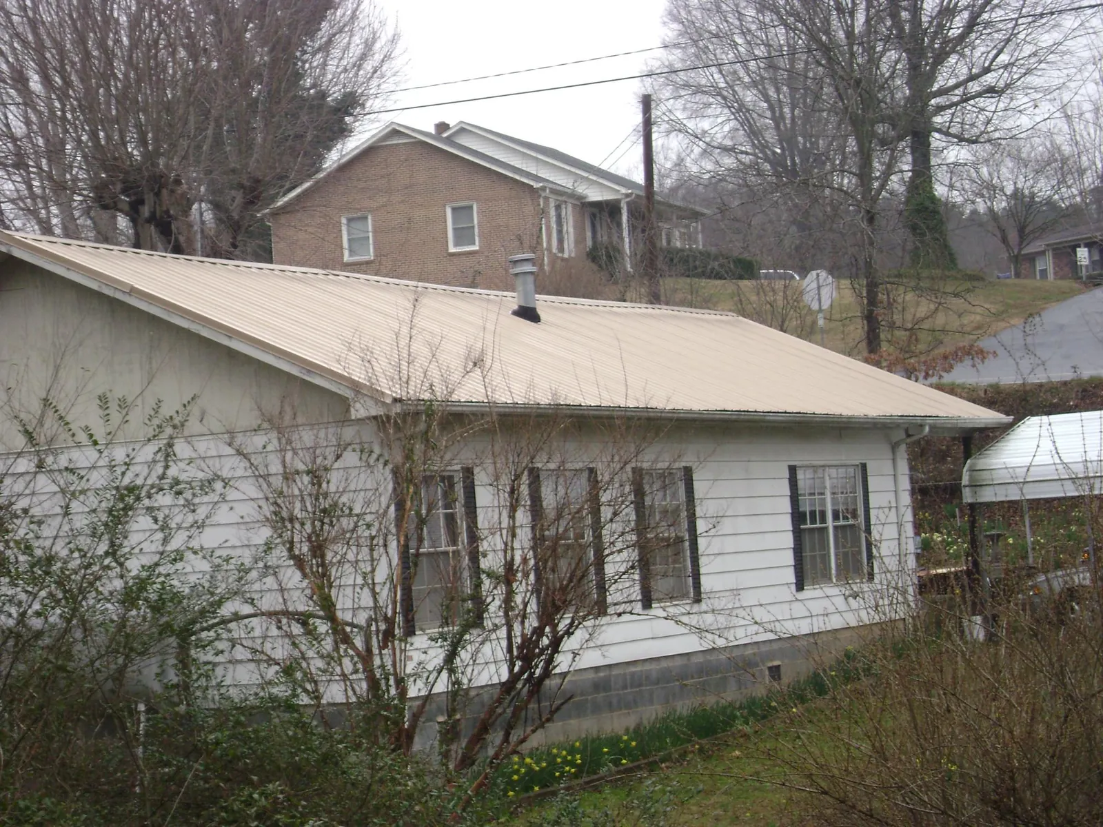 Tan metal roof on a white sided house set into a hillside — Commercial Roofing by Roofing Brothers in Pitsburg